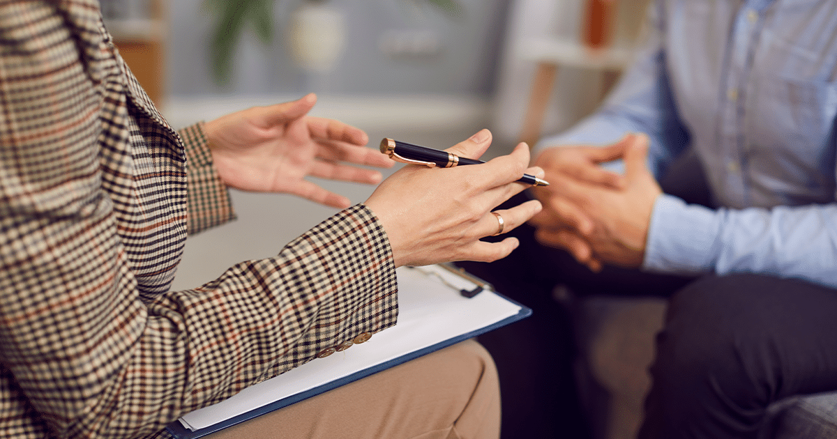 Hands holding a pen with a clipboard on the lap.